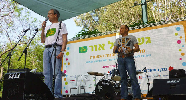 על הבמה: לייזי אורן, נשיא "גשר של אור", מברך את האורחים בשם הפרויקט. לצדו פלי הנמר, יזם ומנהיג קבוצת אנשים ומחשבים והמנחה המסורתי של הטקס